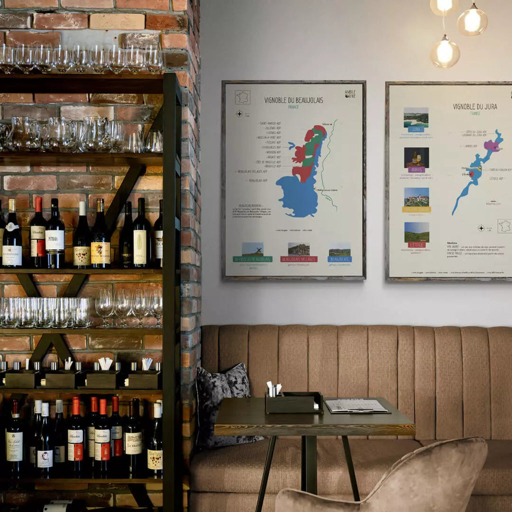 Vous voyez la carte Amble Wine du vignoble du Beaujolais et la carte Amble Wine du vignoble du Jura, tous les deux sont accrochés au mur d'un restaurant. On voit également une table et un canapé en cuir beige.
